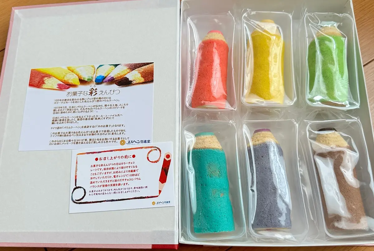 【メルヘン日進堂】は、石川県珠洲市に本店を構える和洋菓子店です。 大正2年創業の老舗で、2024年に創業111周年を迎えました。バームクーヘンを中心に、地域の特産品を活かしたお菓子作りを行っており、添加物を使わないなど健康にも配慮しています！✨  特にバームクーヘンは独創的で、いろえんぴつや、ビールジョッキの形をしたもの、五色五層のカラフルな「大地の虹」などが人気です！🌈