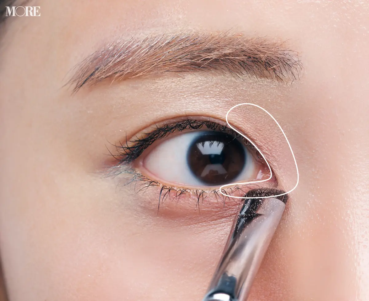 ピンクのアイシャドウがついたブラシを目頭に置いた目元